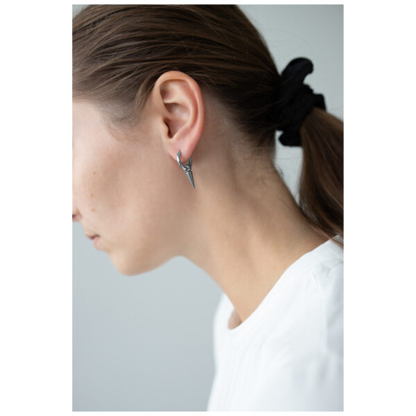 Mujer con pendientes de pinchos plateados, cabello recogido, fondo blanco
