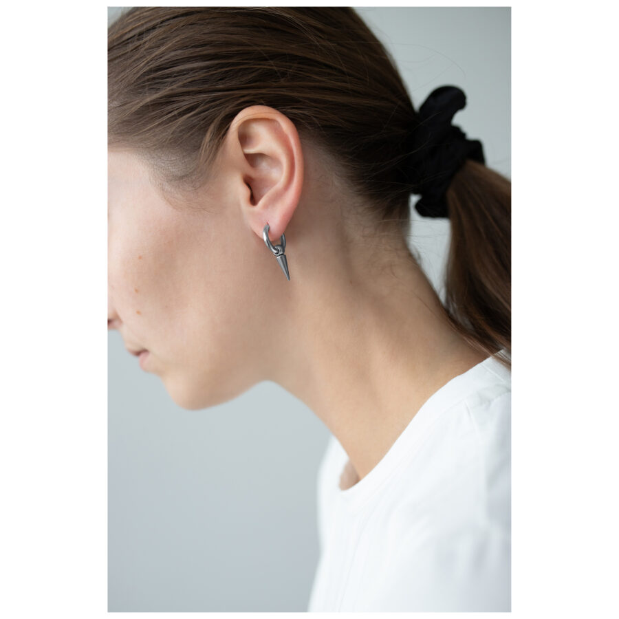 Mujer con pendientes de pinchos plateados, cabello recogido, fondo blanco