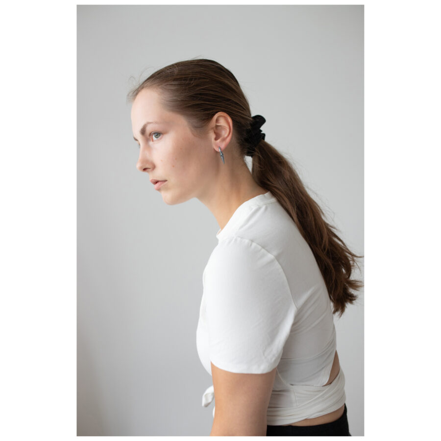 Mujer con cabello largo y liso lleva pendientes de pinchos de acero quirúrgico negro y plateado, camiseta blanca.