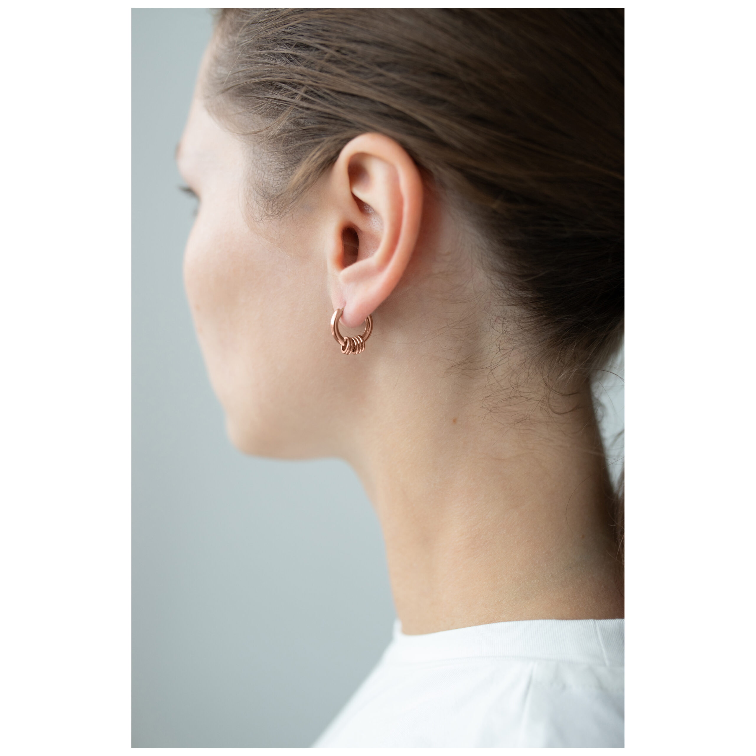 Frau trägt Roségold Little 5 Rings Hoops Ohrringe vor neutralem Hintergrund