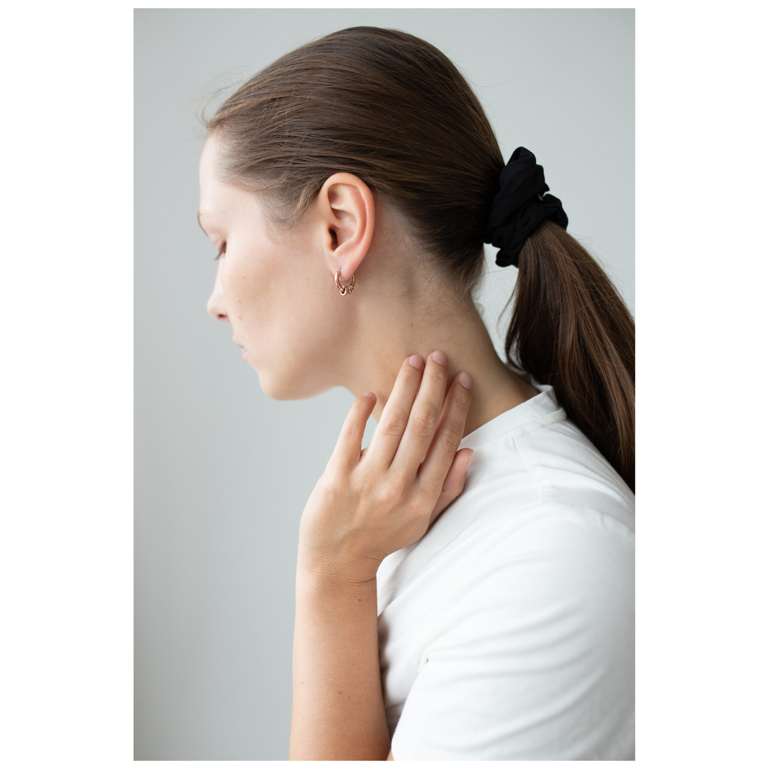 Frau mit braunen Haaren trägt roségoldene Ohrringe auf weißem Hintergrund