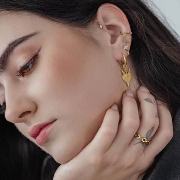 Primer plano de aros de corazón dorados en la oreja de una mujer con cabello oscuro