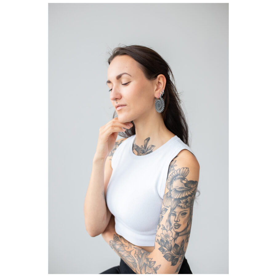 Mujer con brazo tatuado lleva Floral Nautilus Hoops plateados frente a fondo gris
