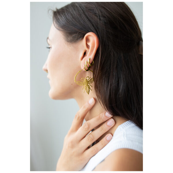 Mujer con pendientes de abejas doradas de acero quirúrgico sobre fondo neutro