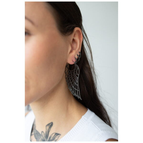 Primer plano de pendientes Wing Hoops negros en una oreja, llevados por una persona con cabello largo y oscuro