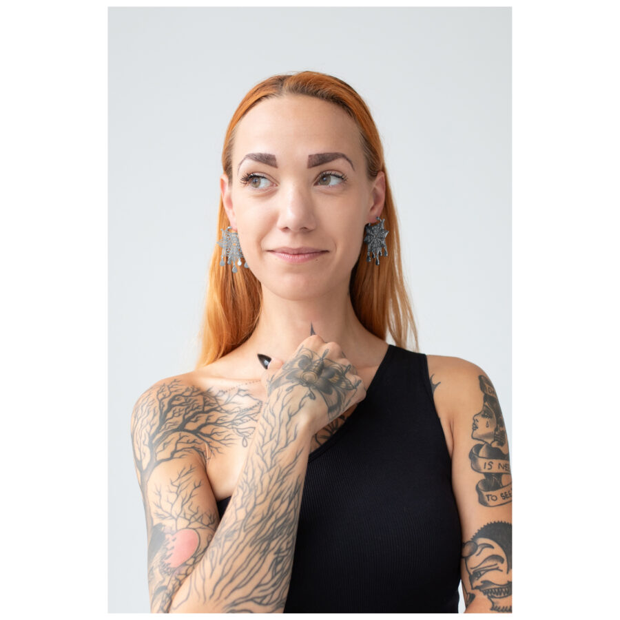 Mujer con cabello rojo lleva aros Mandala plateados, tatuajes visibles