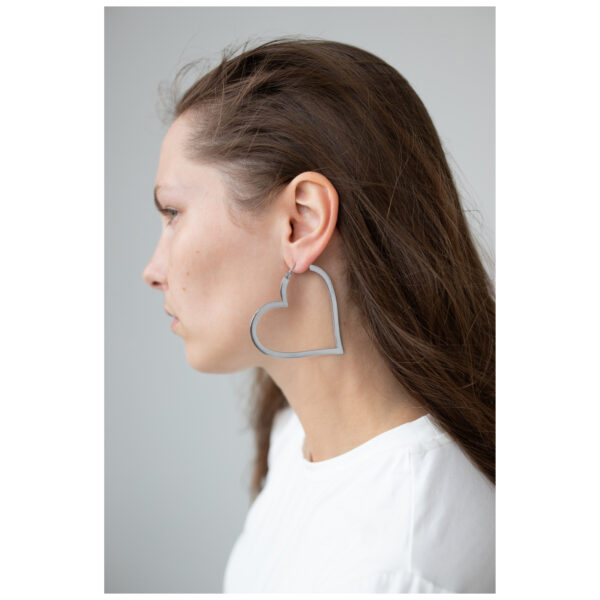Mujer lleva pendientes de corazón plateados, perfil lateral