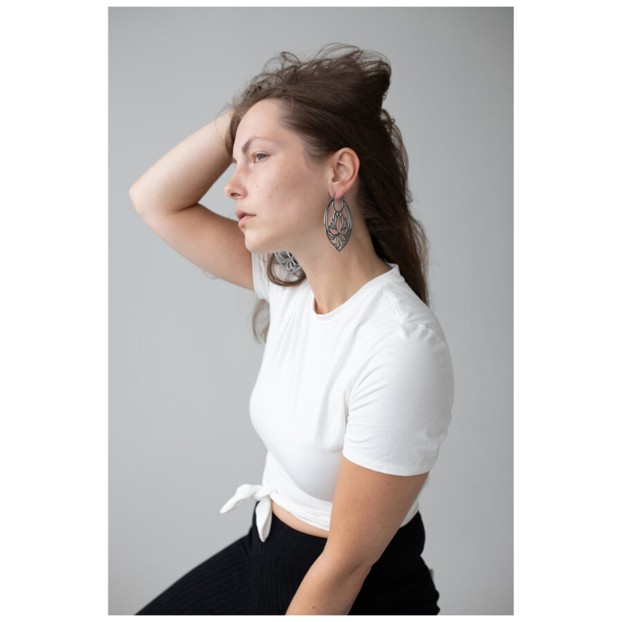 Mujer con pendientes Lotus Hoops de acero inoxidable en negro y plata sobre fondo gris