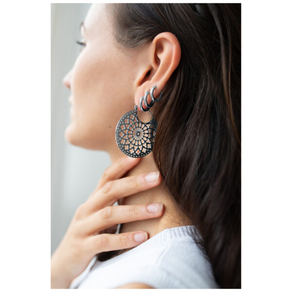 Mujer lleva grandes pendientes redondos en negro-plata con diseño delicado.