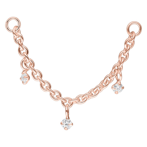 Cadena de piercing en oro rosa con tres colgantes de cristal claro sobre fondo blanco