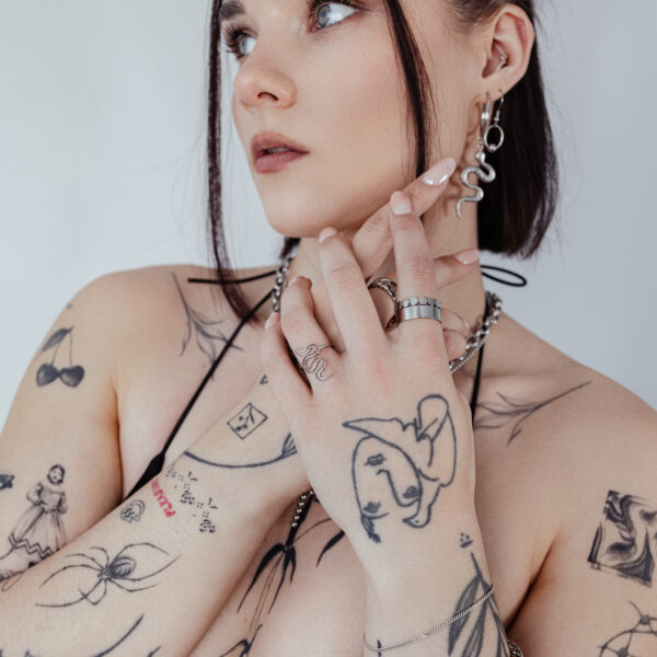 Persona con anillo de serpiente y tatuajes, lleva joyas sobre fondo blanco