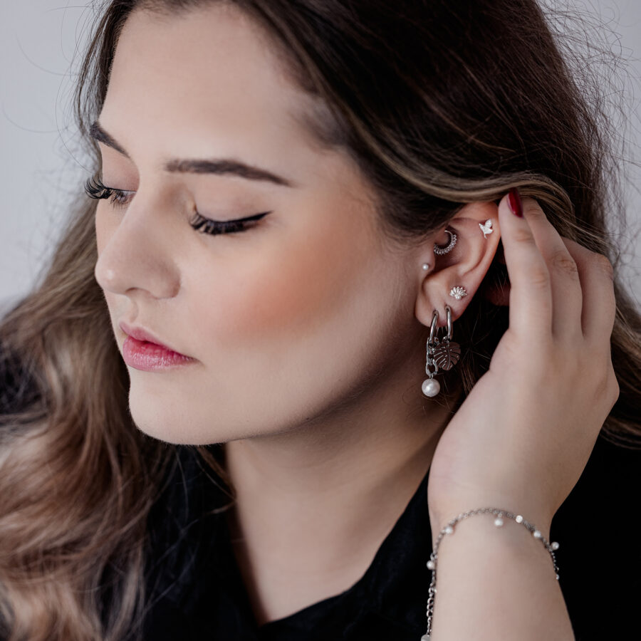 Mujer con Push Fit Pearl Peacock accesorio en la oreja, top negro, piel clara