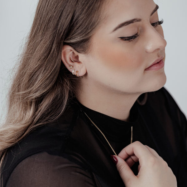 Mujer con piercing en la oreja, pieza dorada Push Fit Crystal Lovely Eye, camiseta negra