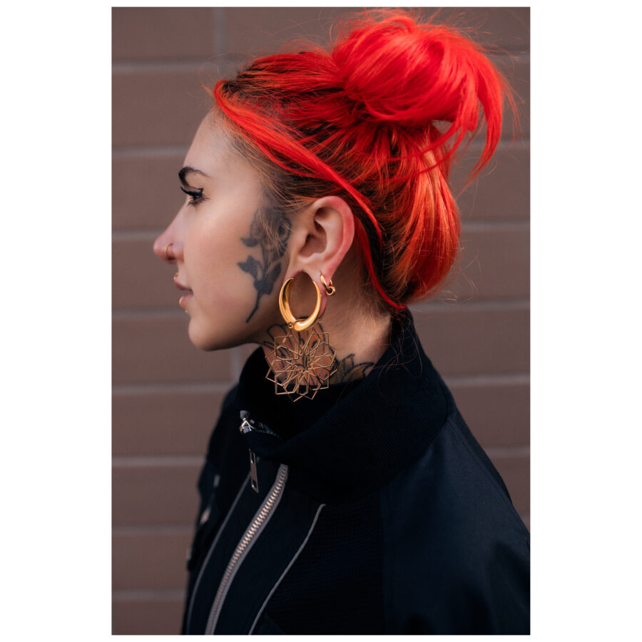 Mujer pelirroja lleva Kaleidoscope Hoops dorados frente a una pared de ladrillo