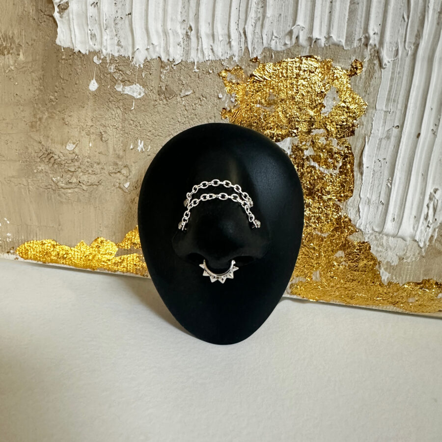 Cadena de piercing plateada en soporte negro frente a pared dorada y blanca