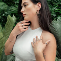 Mujer lleva pendientes de metal negro con chapas sobre fondo verde