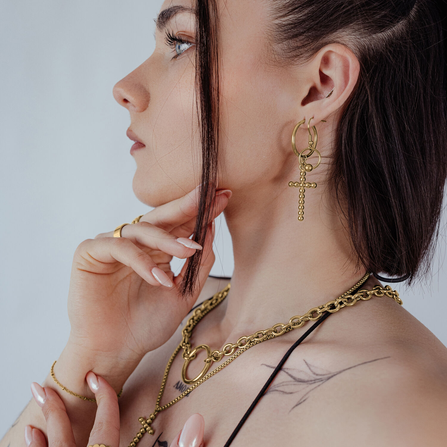 Frau mit goldenen Bubble Cross Hoops Ohrringen vor hellem Hintergrund