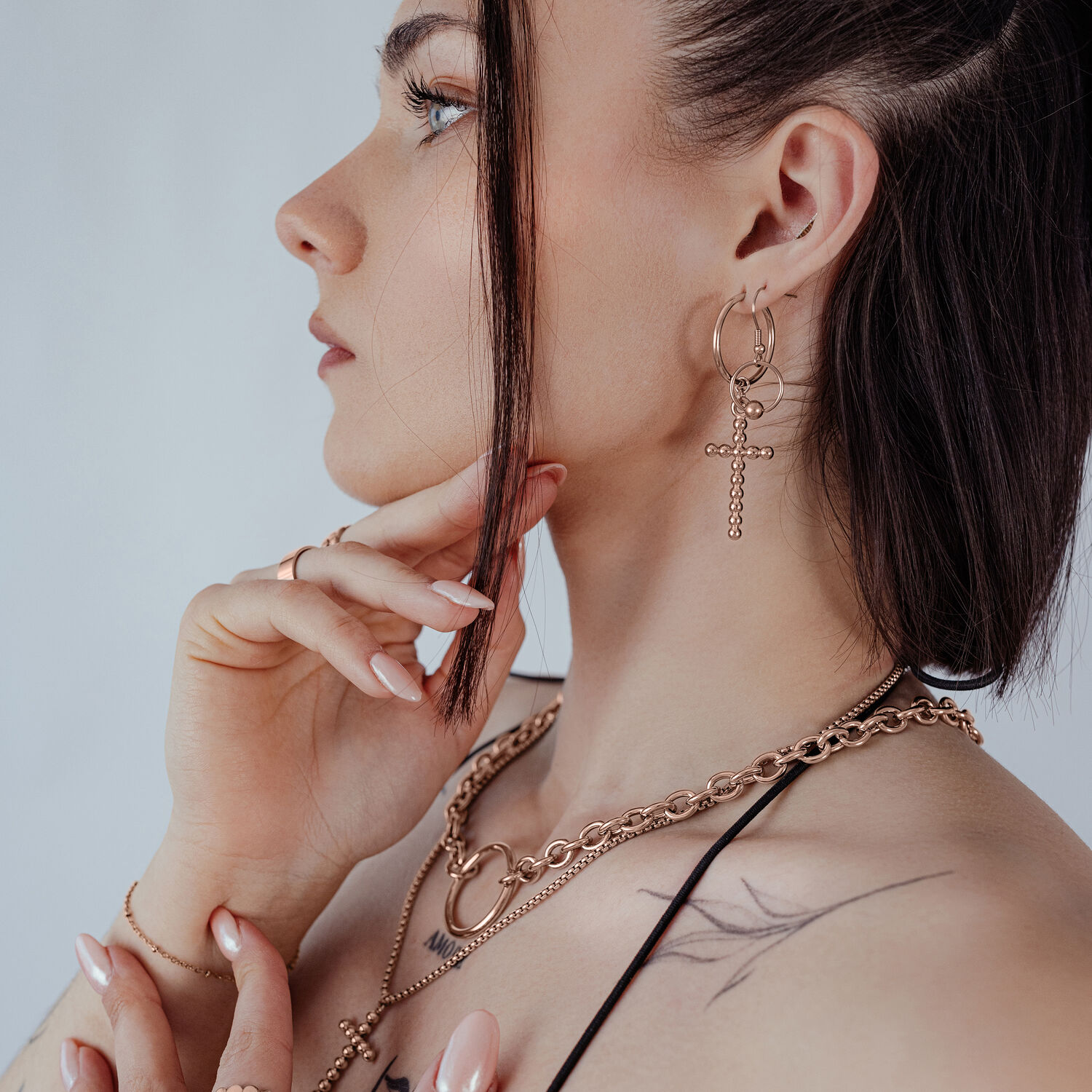 Frau trägt roségoldene Bubble Cross Hoops Ohrringe vor neutralem Hintergrund