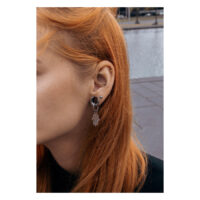 Silberfarbene Hamsa Hand Ohrringe an einem Ohr mit langem roten Haar, draußen aufgenommen