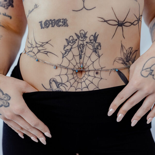 Mujer lleva cadenas dobles plateadas y doradas en el vientre tatuado