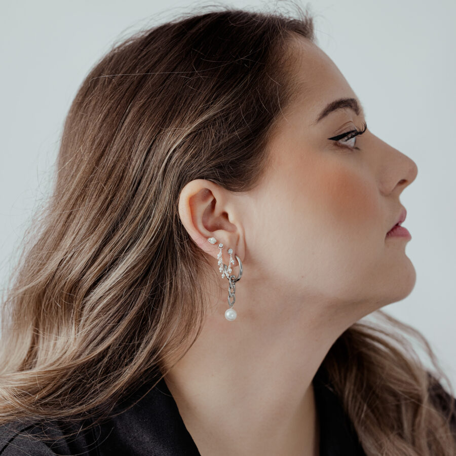 Mujer con cadena de piercing plateada en la oreja, cabello hacia un lado, fondo claro