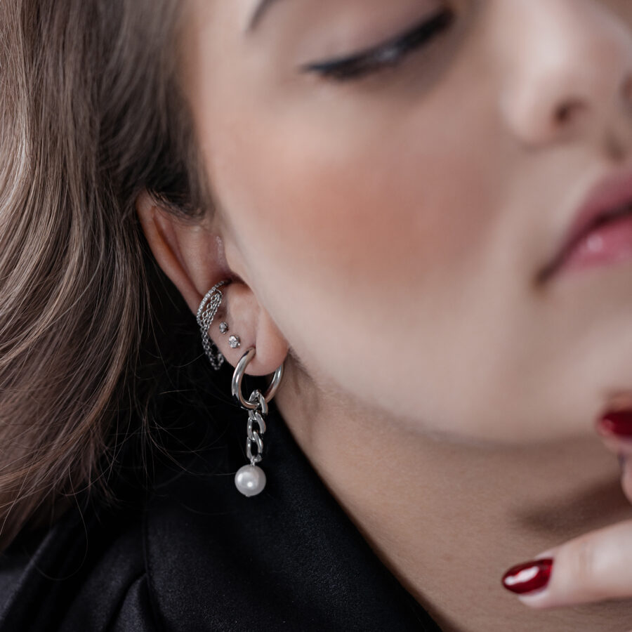 Primer plano de aros de plata con colgante de perla en la oreja de una persona