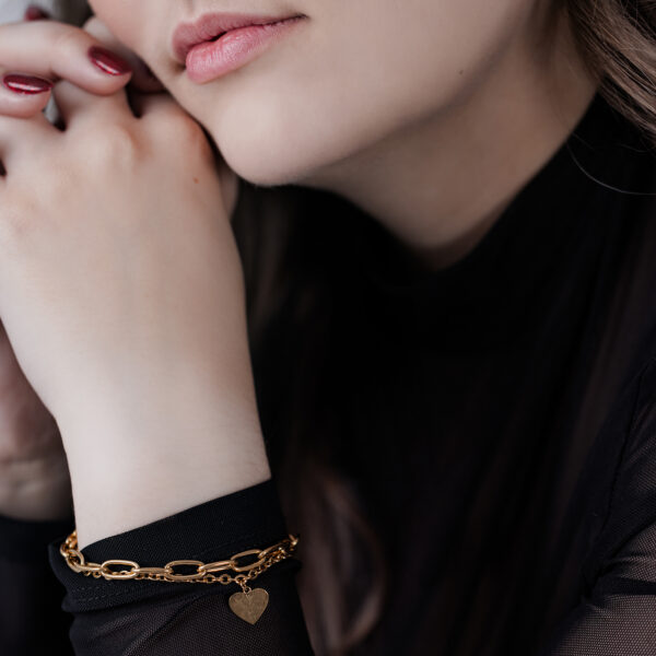 Mujer con pulsera de corazón dorada sobre fondo negro