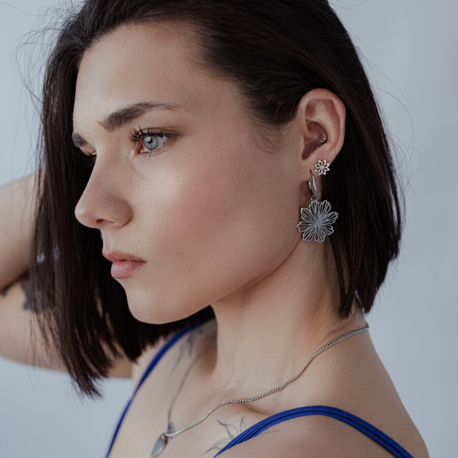 Mujer con pelo corto lleva Fine Flower Hoops de plata sobre fondo gris