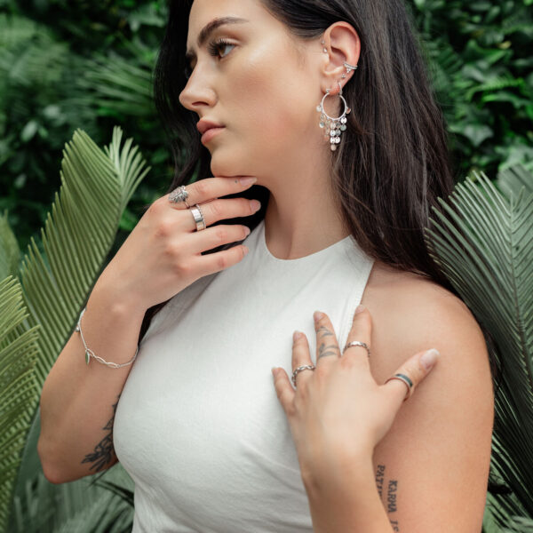 Mujer con elegantes pendientes colgantes de acero quirúrgico en un entorno tropical