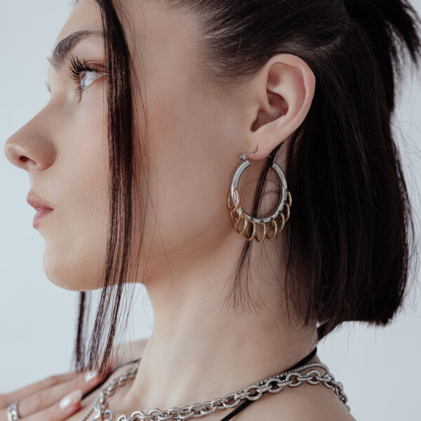 Mujer con aros elegantes y masivos con loops en plata y oro sobre fondo blanco