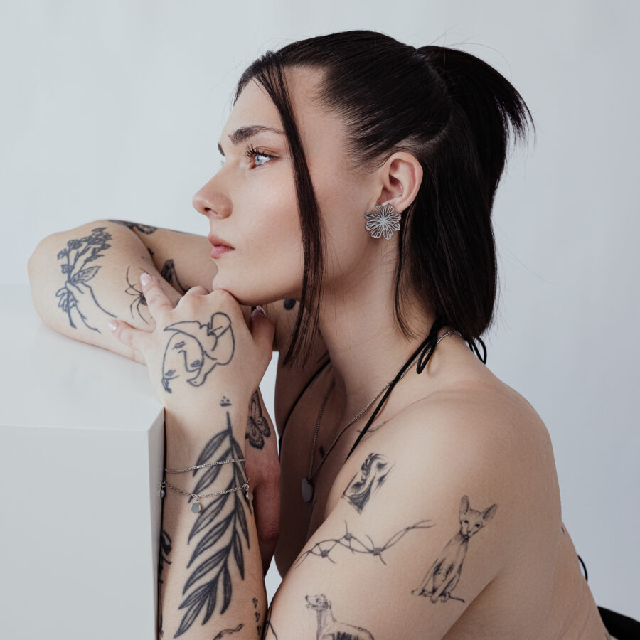 Retrato lateral de una persona tatuada con elegantes pendientes de flor, fondo neutro