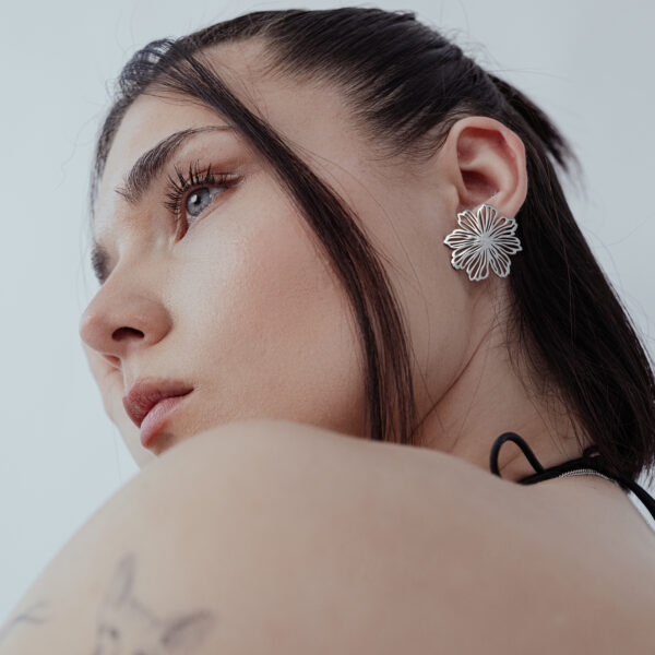 Mujer con elegantes pendientes de flores de acero inoxidable plateado sobre fondo blanco