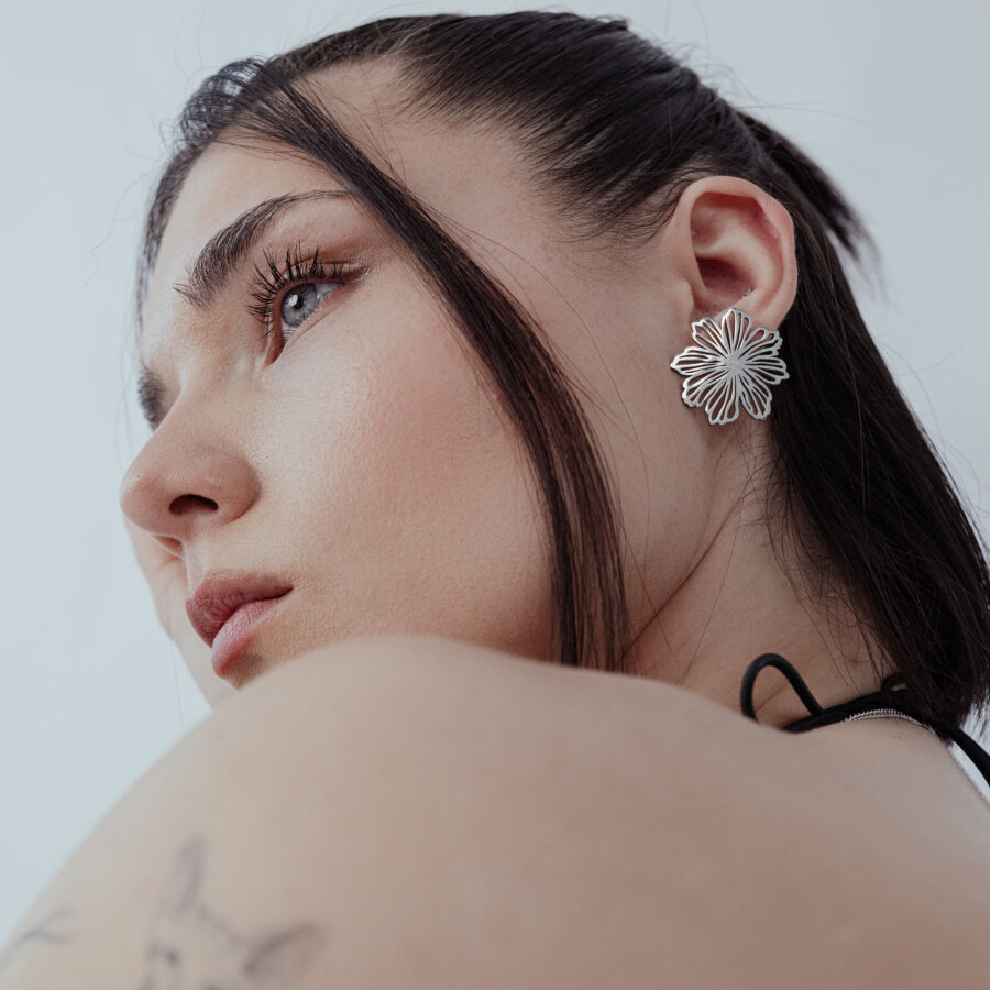Mujer con elegantes pendientes de flores de acero inoxidable plateado sobre fondo blanco