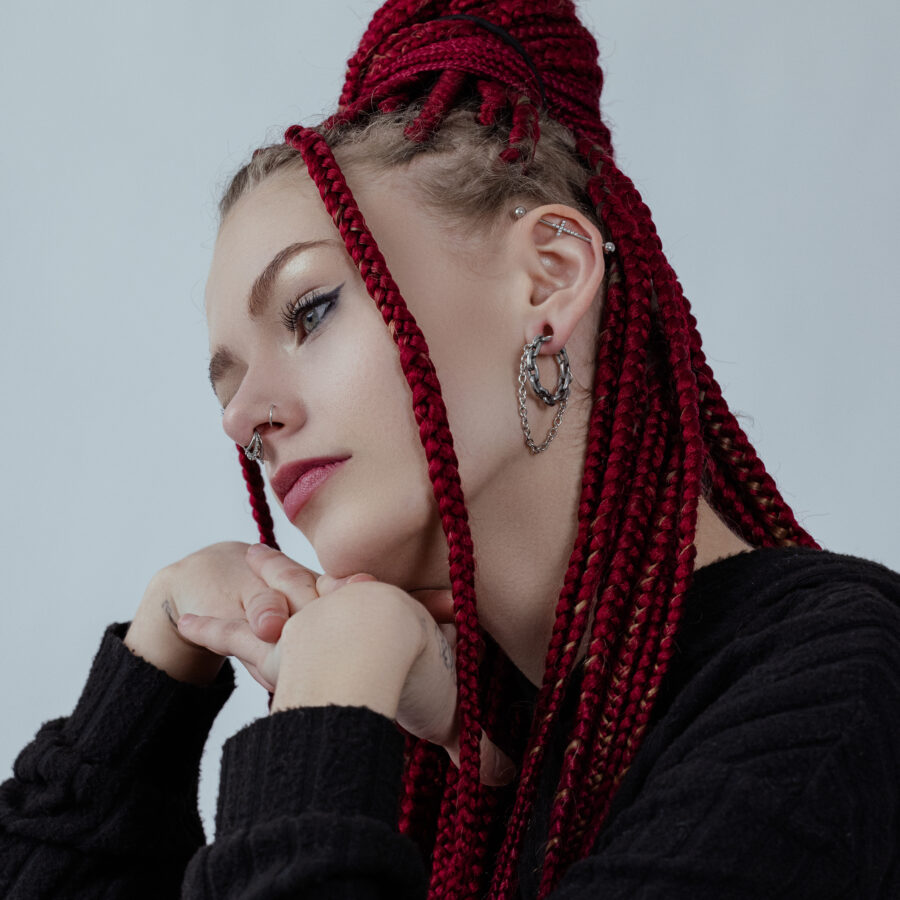 Mujer con trenzas rojas lleva pesos para orejas Double Chain en plata y suéter negro frente a fondo gris