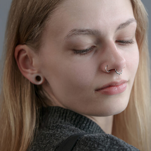 Mujer con clicker septum plateado y lóbulos de las orejas dilatados sobre fondo gris