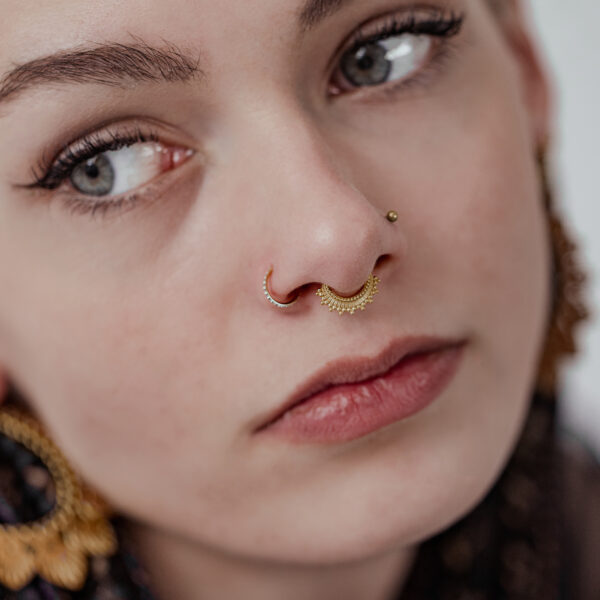 Primer plano de un rostro con clicker de septum dorado y pendiente