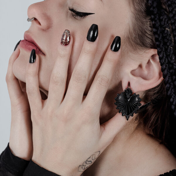 Mujer con pesas para orejas Sacred Heart negras y esmalte de uñas negro, vista lateral