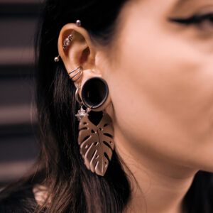 Silberfarbene Monstera-Ohrringe aus Chirurgenstahl, getragen am Ohr einer Frau, vor dunklem Hintergrund