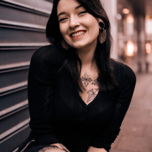 Frau mit Monstera Leaf Ohrringen aus silberfarbenem Metall vor städtischem Hintergrund