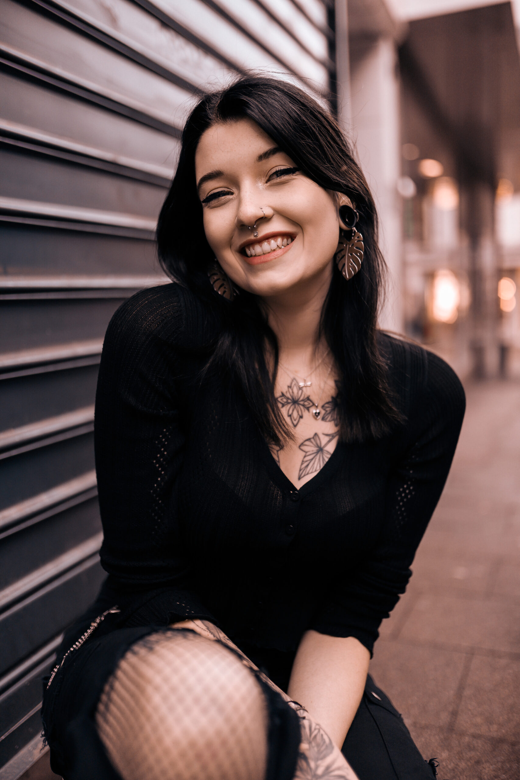 Frau mit Monstera Leaf Ohrringen aus silberfarbenem Metall vor städtischem Hintergrund