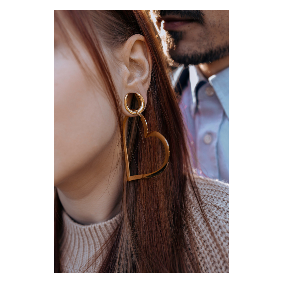 Herz Creolen Roségold im Ohr getragen Roségoldene Herz Creolen am Ohr einer Frau, im Hintergrund ein Mann