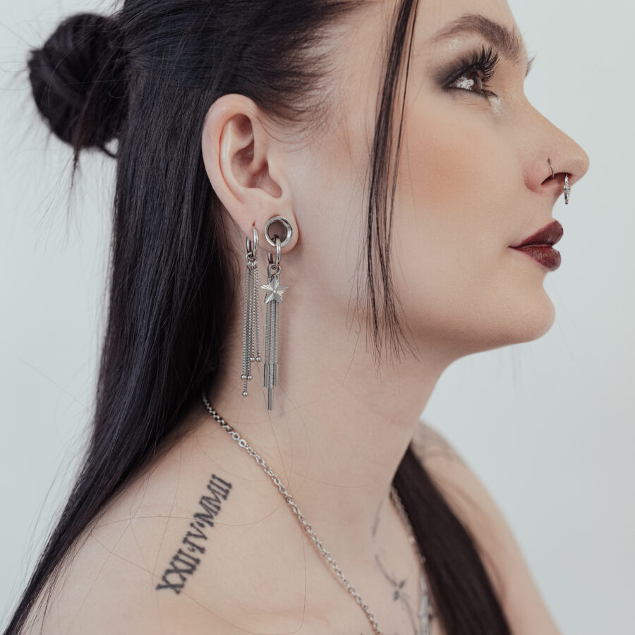 Mujer con cabello largo y negro lleva aros Little Shooting Star plateados y tiene tatuajes en el cuello.