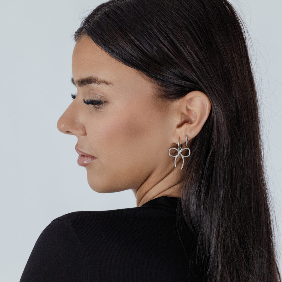 Mujer con Little Twisted Bow Hoops plateados frente a un fondo claro
