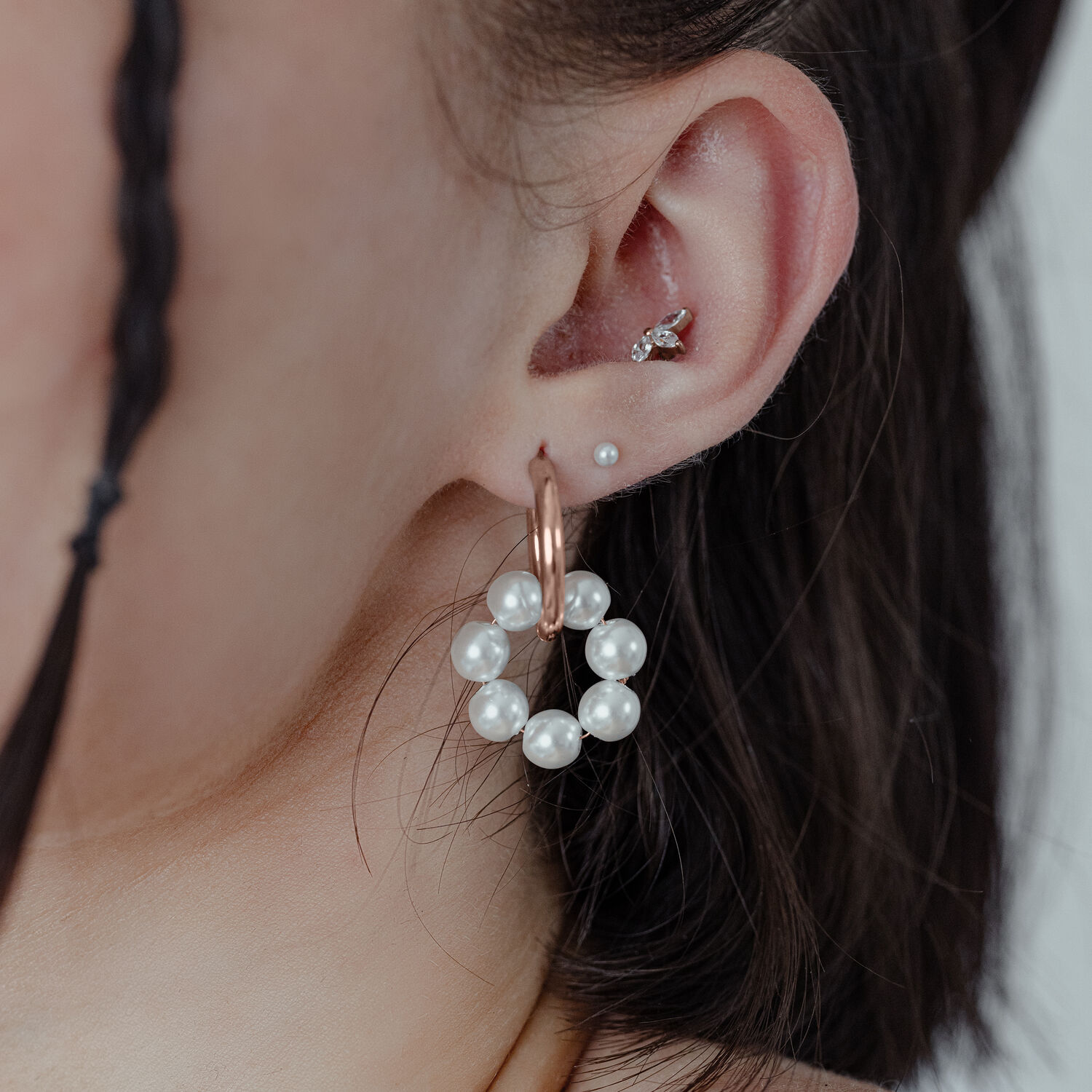 Roségoldene Creolen mit Perlen an einem Ohr auf neutralem Hintergrund