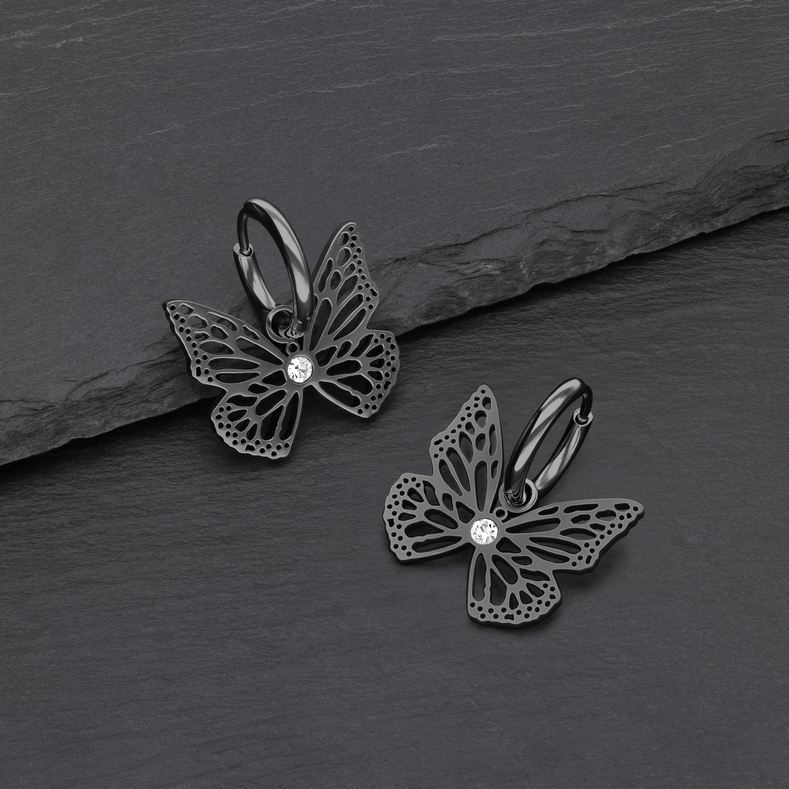 Pendientes de mariposa negros de acero quirúrgico con cristal claro sobre fondo gris