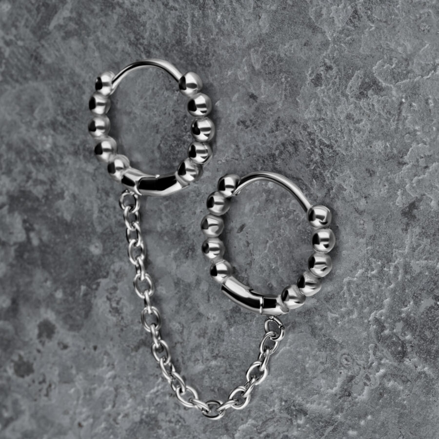 Pendientes Huggie dobles de plata con bolas y cadena sobre fondo gris