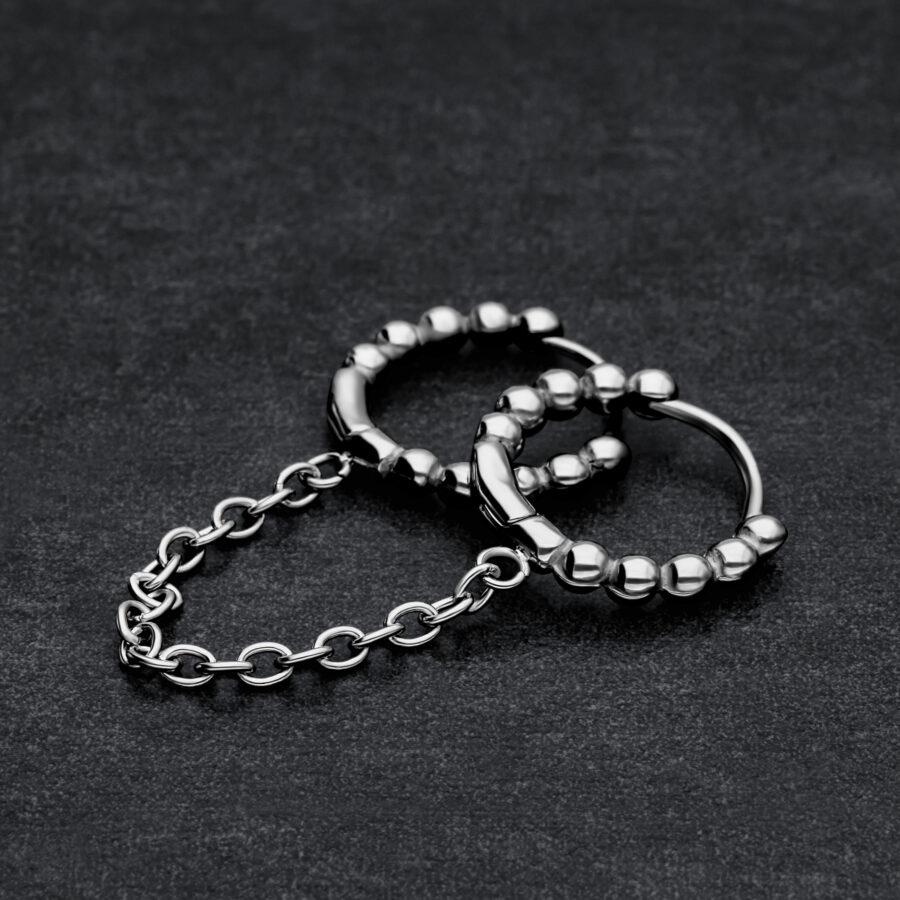 Dos aros Huggie negros conectados con bolas sobre fondo oscuro