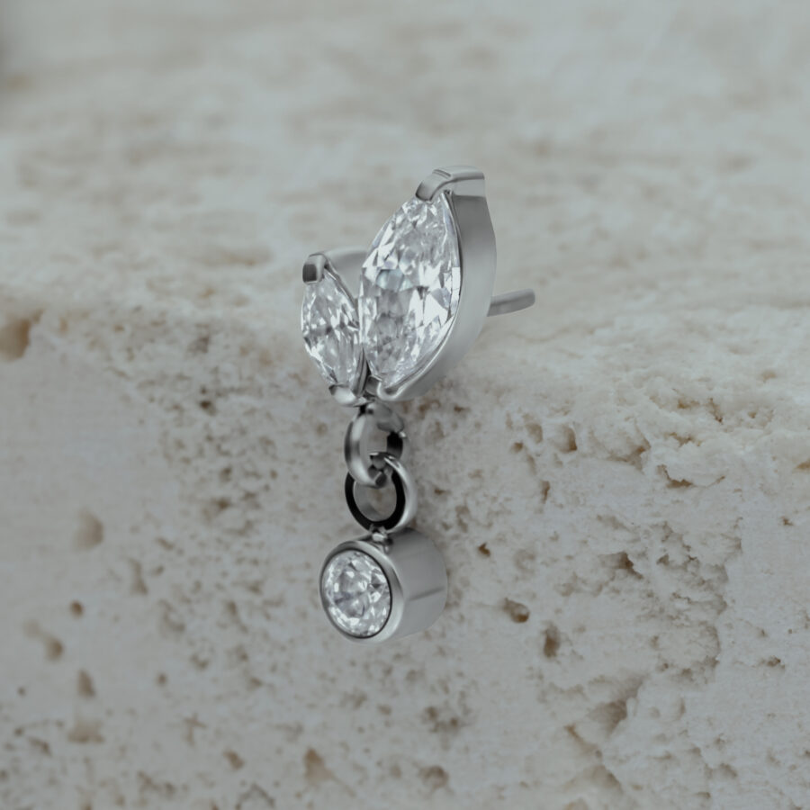 Accesorio de piercing plateado con dos cristales en forma de marquesa y un cristal colgante sobre piedra