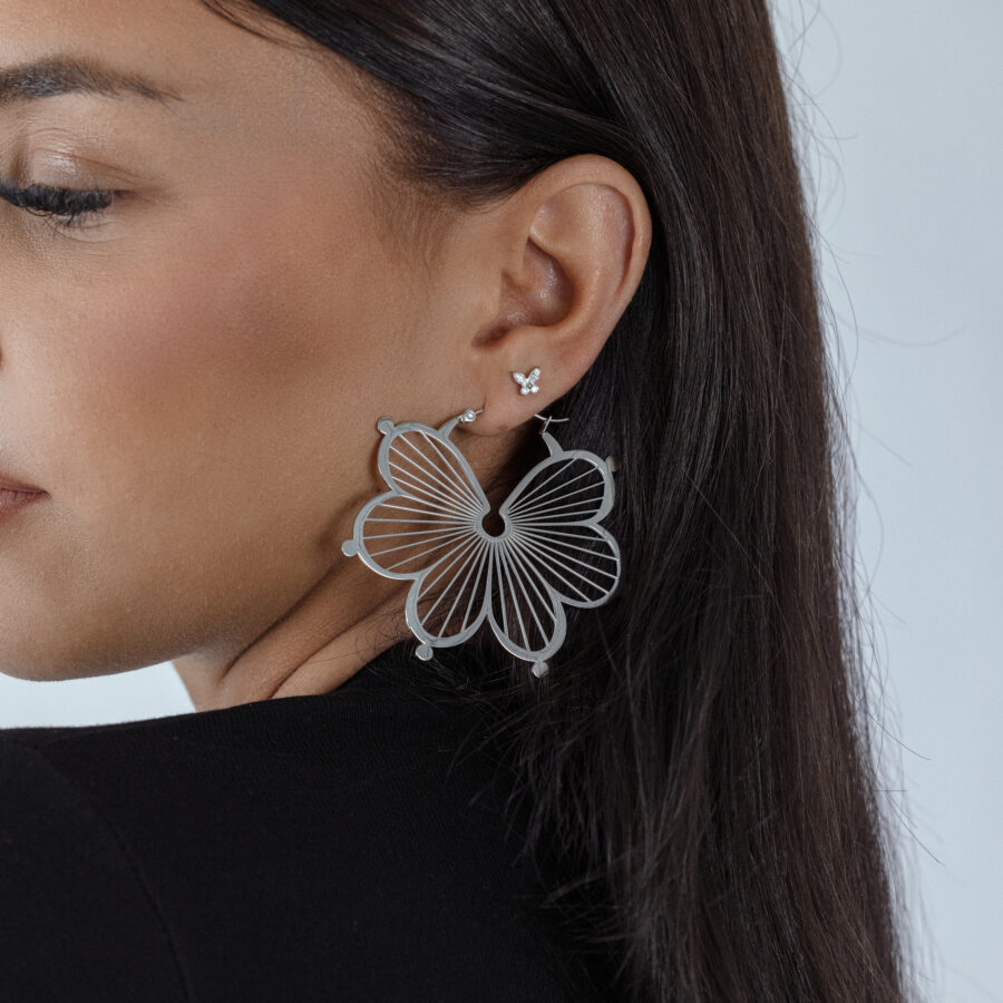 Mujer con un gran adorno de mariposa plateado en la oreja, fondo negro