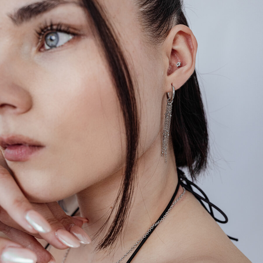 Mujer con punta de flor Push Fit en la oreja, cadena y pendientes plateados, fondo blanco
